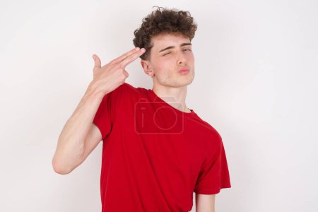 Foto de Joven guapo infeliz imita disparo de arma hace gesto suicida mantiene dos dedos en las sienes. - Imagen libre de derechos