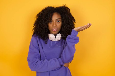 Téléchargez les photos : Portrait de jeune femme afro-américaine expressive avec écouteurs sur fond jaune - en image libre de droit