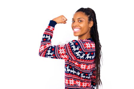 Photo for African American woman wearing Christmas sweater against white wall  showing muscles after workout. Health and strength concept. - Royalty Free Image