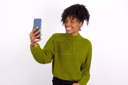 Isolated shot of pleased cheerful young woman, makes selfie with mobile phone. People, technology and leisure concept