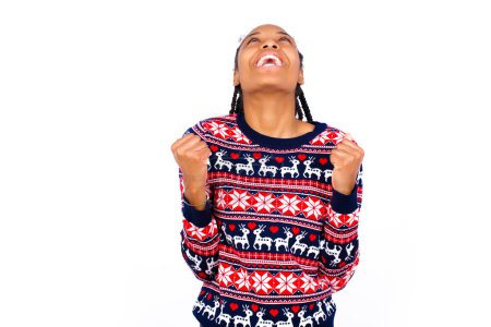 Photo for African American woman wearing Christmas sweater against white wall looks with excitement up, keeps hands raised, notices something unexpected. - Royalty Free Image