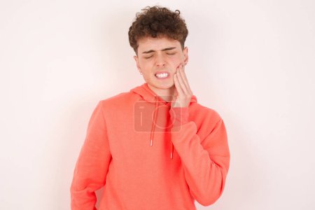Téléchargez les photos : Concept de mal de dent. Plan intérieur de la douleur ressentie par le jeune homme, tenant sa joue avec la main, souffrant de mal de dents, regardant la caméra avec une expression douloureuse - en image libre de droit
