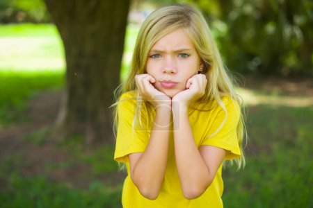Téléchargez les photos : Portrait de triste petite fille caucasienne portant t-shirt jaune debout mains extérieures visage - en image libre de droit