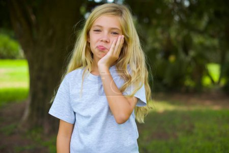Photo for Sad lonely pretty girl touches cheek with hand bites lower lip and gazes with displeasure. Bad emotions - Royalty Free Image