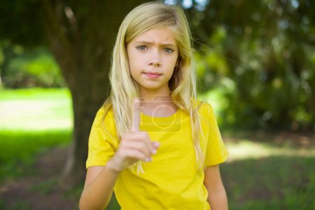 Foto de Niña caucásica vistiendo camiseta amarilla de pie al aire libre frustrada y señalando hacia el frente - Imagen libre de derechos