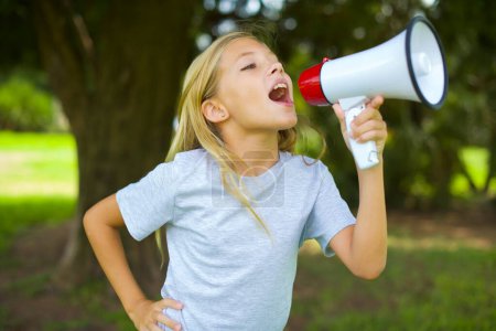 Photo for Funny caucasian little girl wearing white t-shirt standing outdoors People sincere emotions lifestyle concept. Mock up copy space. Screaming in megaphone. - Royalty Free Image