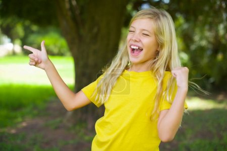 Téléchargez les photos : Joyeux caucasien petite fille portant jaune t-shirt debout à l'extérieur montrant copie espace annonce célébrant la chance - en image libre de droit