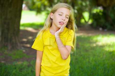 Téléchargez les photos : Petite fille caucasienne portant t-shirt jaune debout à l'extérieur avec mal de dents - en image libre de droit