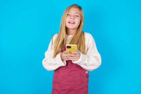 Téléchargez les photos : Souriant adolescent fille amical et heureux tenant téléphone mobile - en image libre de droit