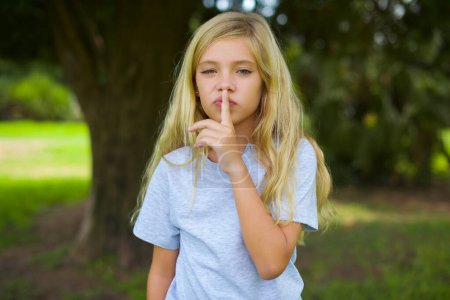 Photo for Surprised pretty girl makes silence gesture, keeps finger over lips and looks mysterious at camera - Royalty Free Image