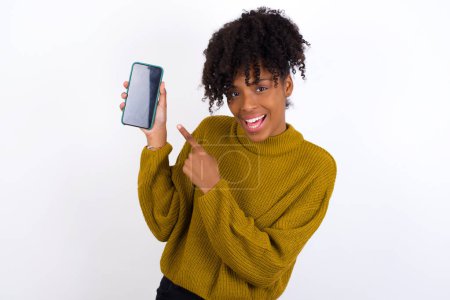 Téléchargez les photos : Jeune femme excitée tenant et pointant du doigt le smartphone avec écran blanc. Concept de publicité. - en image libre de droit