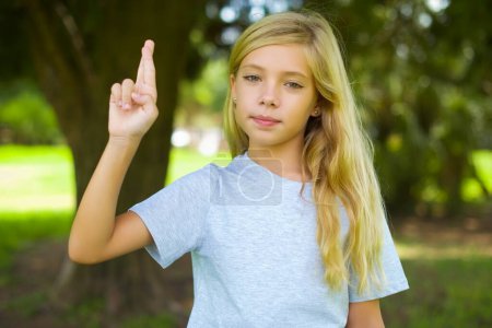 Téléchargez les photos : Adolescent jolie fille montrant croisé doigts geste dans parc - en image libre de droit
