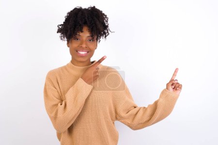 Foto de Mujer joven positiva con sonrisa radiante apuntando con dos dedos y mirando en espacio de copia vacío. Concepto de publicidad. - Imagen libre de derechos