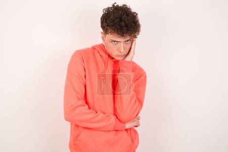 Photo for Very bored handsome young man holding hand on cheek while support it with another crossed hand, looking tired and sick. - Royalty Free Image