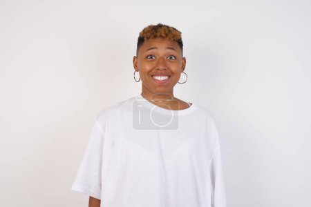 Photo for Young beautiful African American woman wearing white t-shirt with an afro hairstyle having broad white smile being excited to meet Friends and go out to have a good day. - Royalty Free Image