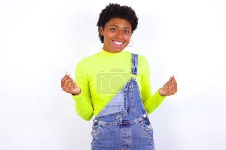 Foto de Joven mujer afroamericana con el pelo corto con denim en general contra blanco haciendo gesto de dinero. - Imagen libre de derechos