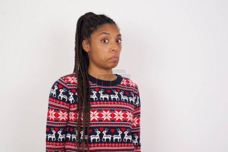 Foto de Mujer afroamericana vistiendo jersey navideño contra pared blanca con expresión esnob curvando labios y levantando cejas, mirando con expresión dudosa y escéptica, sospechosa y dudosa. - Imagen libre de derechos