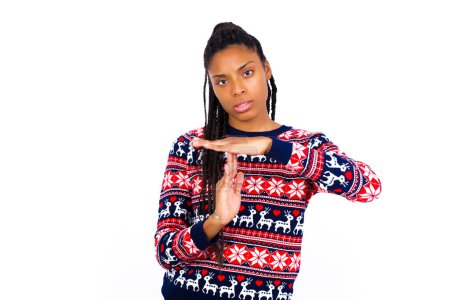 Foto de Mujer afroamericana vistiendo suéter de Navidad contra la pared blanca se siente cansado y aburrido, haciendo un gesto de tiempo de espera, tiene que parar debido al estrés laboral, concepto de tiempo. - Imagen libre de derechos