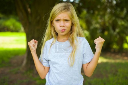 Photo for Irritated pretty girl blows cheeks with anger and raises clenched fists expresses rage and aggressive emotions. Furious model - Royalty Free Image