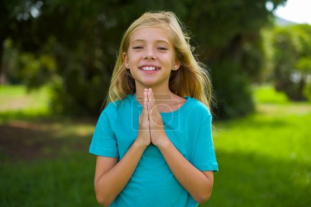 retrato de hermosa niña caucásica usando camiseta azul de pie al aire libre en el parque