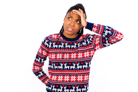 Photo for African American woman wearing Christmas sweater against white wall touching forehead, hears something surprising, glad receive good news, feels relieved. Almost got in trouble. - Royalty Free Image