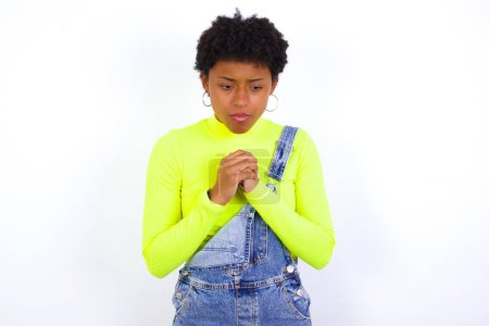 Photo for Sad young African American woman with short hair wearing denim overall against white feeling upset while spending time at home alone staring at camera with unhappy or regretful look. - Royalty Free Image