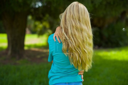 Téléchargez les photos : Portrait de belle petite fille caucasienne portant t-shirt bleu debout en plein air dans le parc, vue de dos - en image libre de droit