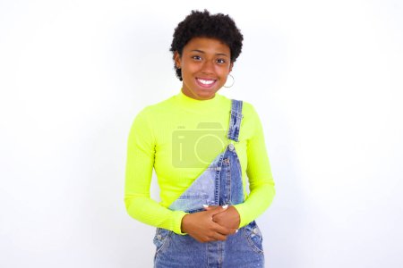 Foto de Business Concept - Retrato de una joven afroamericana con el pelo corto usando denim en general contra la pared blanca tomados de la mano con la cara segura. - Imagen libre de derechos