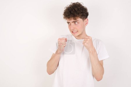 Photo for Handsome young man over white background clenches fists and awaits for something nice happened looks away bites lips and waits announcement of results - Royalty Free Image
