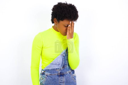 Foto de Joven mujer afroamericana con el pelo corto con denim en general contra la pared blanca con expresión triste que cubre la cara con las manos mientras llora. Concepto de depresión. - Imagen libre de derechos
