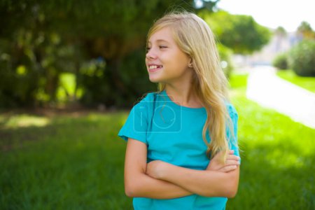 Téléchargez les photos : Portrait de belle petite fille caucasienne portant t-shirt bleu debout en plein air dans le parc se sentant heureux - en image libre de droit
