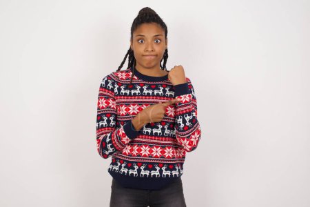 Téléchargez les photos : Femme afro-américaine portant un pull de Noël contre un mur blanc pressé pointant vers regarder le temps, l'impatience, bouleversé et en colère pour retard de délai - en image libre de droit