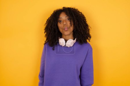 Foto de Retrato de joven mujer afroamericana expresiva con auriculares sobre fondo amarillo - Imagen libre de derechos