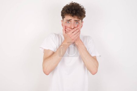 Photo for Stunned handsome young man over white background covers mouth with both hands being afraid from something or after hearing stunning gossips. - Royalty Free Image