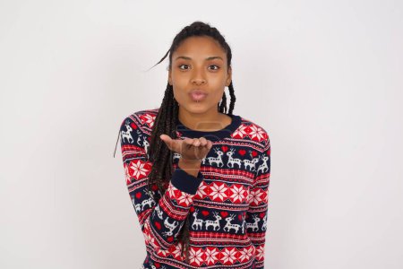 Photo for African American woman wearing Christmas sweater against white wall looking at the camera blowing a kiss with hand on air being lovely and sexy. Love expression. - Royalty Free Image
