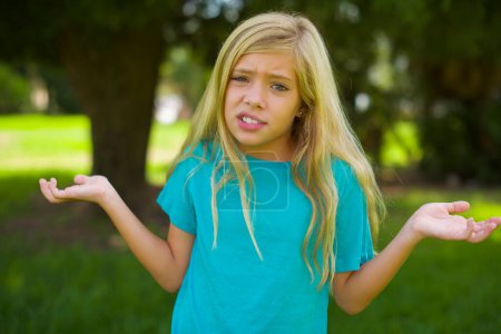 Foto de Retrato de hermosa niña caucásica usando camiseta azul de pie al aire libre en el parque - Imagen libre de derechos