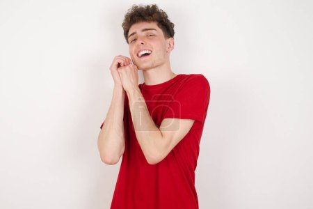 Photo for Dreamy handsome young man over white background with pleasant expression, closes eyes, keeps hands crossed near face, thinks about something pleasant - Royalty Free Image