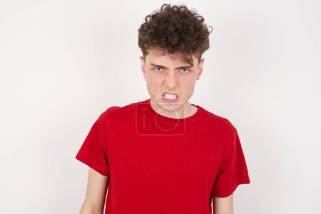 Photo for Mad crazy handsome young man over white background clenches teeth angrily, being annoyed with coming noise. Negative feeling concept. - Royalty Free Image
