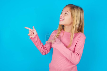Photo for Optimistic pretty girl points with both hands and  looking at empty space. - Royalty Free Image