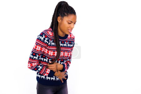 Téléchargez les photos : Femme afro-américaine portant un pull de Noël contre un mur blanc souffrant de fortes douleurs à l'estomac. - en image libre de droit