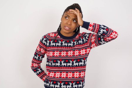 Photo for African American woman wearing Christmas sweater against white wall touching forehead, hears something surprising, glad receive good news, feels relieved. Almost got in trouble. - Royalty Free Image