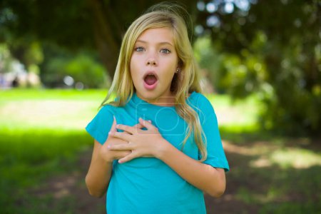 Photo for Portrait of beautiful caucasian little kid girl wearing blue t-shirt standing outdoor in the park have a heart attack - Royalty Free Image