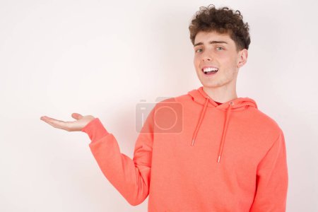 Photo for Positive glad handsome young man over white background says: wow how exciting it is, has amazed expression, shows something on blank space with open hand. Advertisement concept. - Royalty Free Image