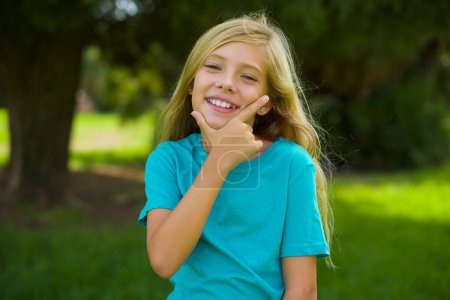 portrait of beautiful caucasian little kid girl wearing blue t-shirt standing outdoor in the park