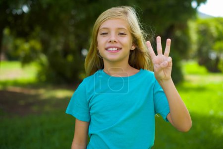 Photo for Caucasian little girl wearing blue t-shirt standing outdoors and showing number three symbol - Royalty Free Image