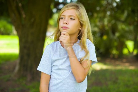 Photo for Thoughtful pretty girl holds chin and looks away pensively makes up great plan - Royalty Free Image
