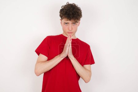 Photo for Handsome young man over white background keeps palms pressed together in front of her having regretful look, asking for forgiveness. Forgive me please. - Royalty Free Image