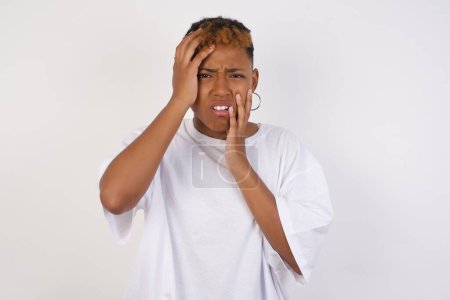 Photo for Young gloomy African American woman wearing white t-shirt hiding her face with hands pouting and crying, standing upset and depressed complaining to friend about her job problems. Her boyfriend forgot about anniversary. - Royalty Free Image