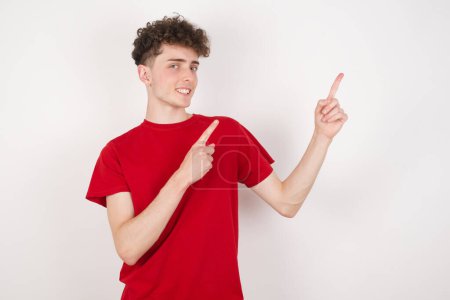 Foto de Joven guapo sobre fondo blanco con expresión positiva, indica con el dedo índice en el espacio de copia en blanco para su texto promocional o anuncio. - Imagen libre de derechos