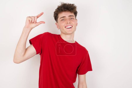 Foto de Joven guapo sobre fondo blanco sonriendo y haciendo gestos con la mano tamaño pequeño, símbolo de la medida. - Imagen libre de derechos